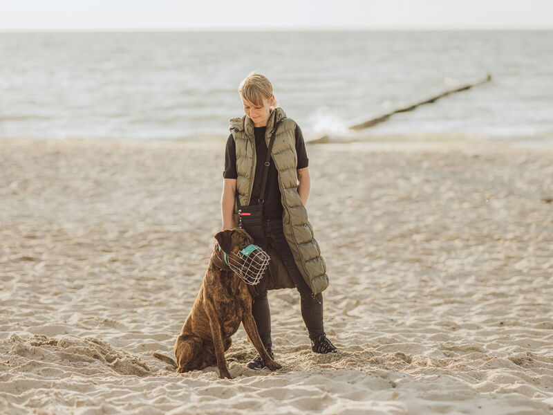 Eine Frau und ein Hund mit Maulkorb stehen am Strand