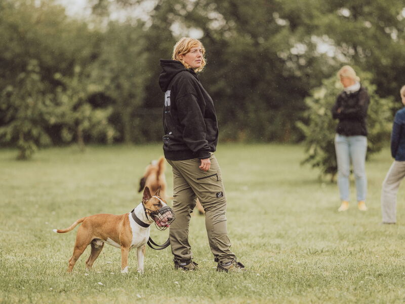 Hundetrainerin Sophia Tumat steht mit einem angeleinten Hund mit Maulkorb auf dem Hundeplatz